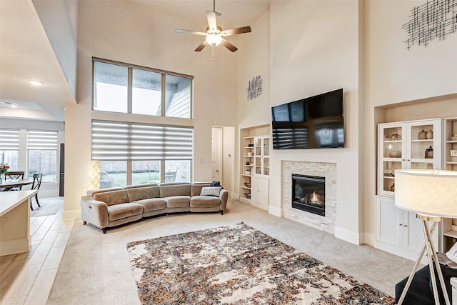 21123 Coral View Dr, Cypress, TX 77433 - living room featuring built in features, a ceiling fan, a towering ceiling, light colored carpet, and a glass covered fireplace