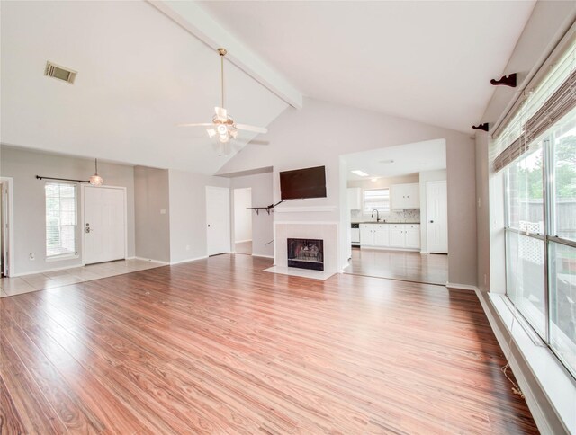 1311 Holly Lake Ct, Katy, TX 77450 - unfurnished living room with a fireplace with flush hearth, light wood finished floors, visible vents, a ceiling fan, and beamed ceiling