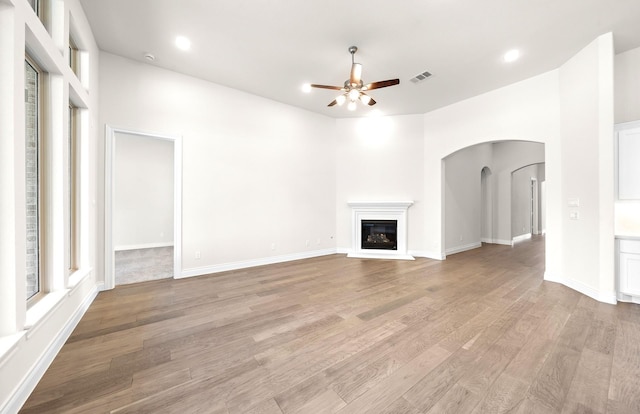 8215 Mount Washburn Ln, Porter, TX 77365 - unfurnished living room with ceiling fan, light wood-type flooring, arched walkways, and a glass covered fireplace