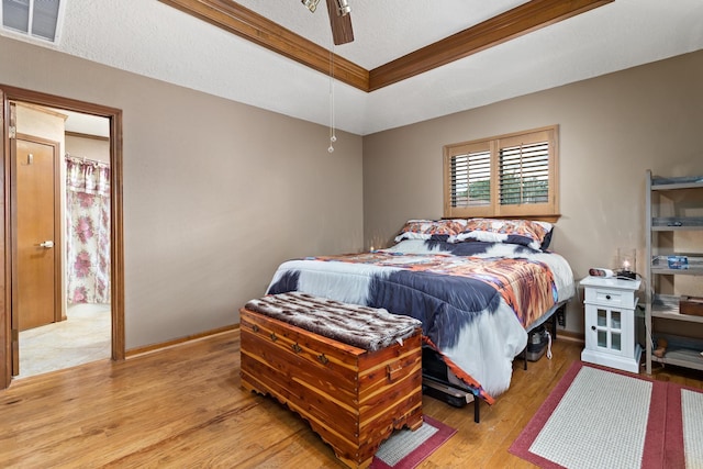 bedroom with a tray ceiling, ornamental molding, visible vents, light wood finished floors, and baseboards