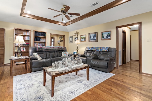 living room with baseboards, visible vents, a tray ceiling, ceiling fan, and wood finished floors