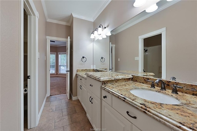 full bath featuring two vanities, baseboards, crown molding, stone finish floor, and a sink