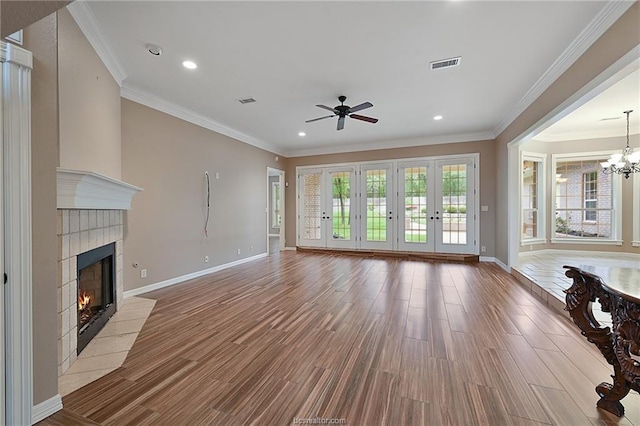 unfurnished living room featuring ceiling fan with notable chandelier, visible vents, wood finished floors, a tile fireplace, and baseboards