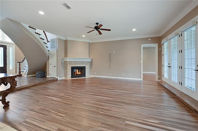 unfurnished living room featuring ornamental molding, light wood-style flooring, a ceiling fan, stairs, and visible vents