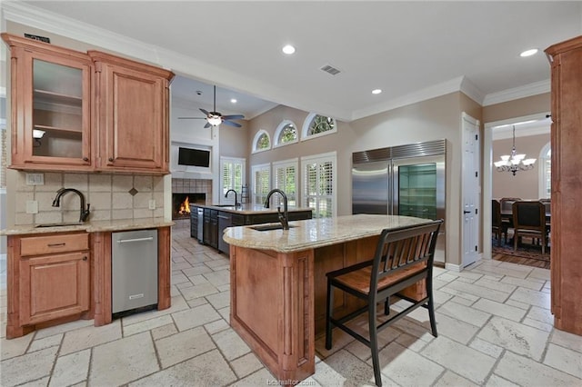 kitchen featuring a fireplace, visible vents, a center island with sink, decorative backsplash, and a sink