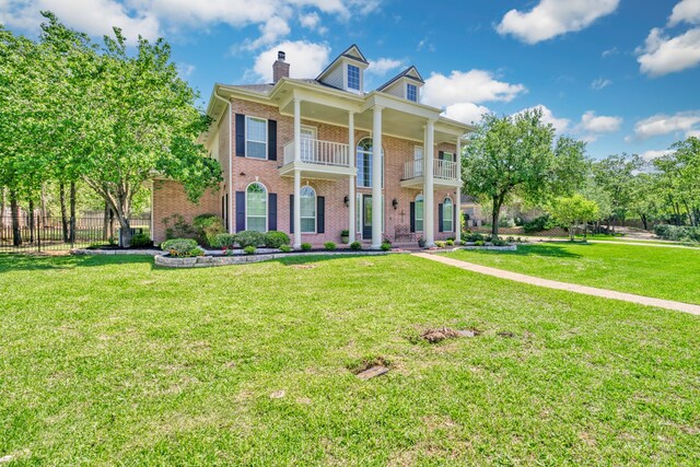 neoclassical home with a front yard, fence, and a balcony