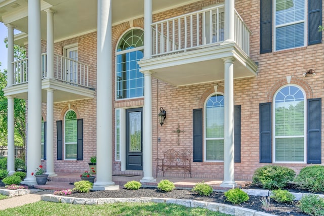 doorway to property with brick siding, a balcony, and covered porch