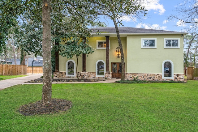 view of front facade with a front yard, stone siding, fence, stucco siding, and french doors