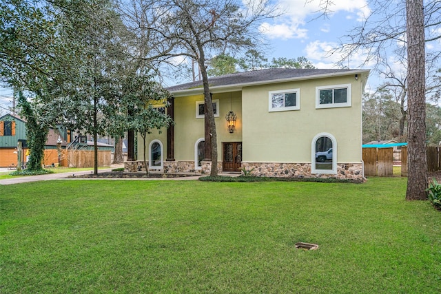 view of front of property with a front yard, fence, stone siding, and stucco siding