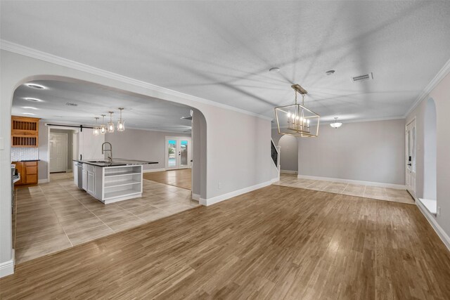 unfurnished dining area featuring light wood-type flooring, an inviting chandelier, ornamental molding, visible vents, and arched walkways