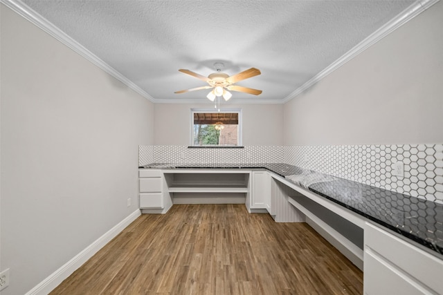 unfurnished office with built in desk, wood finished floors, crown molding, and a ceiling fan
