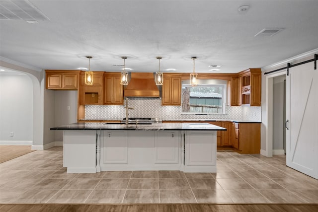 kitchen with brown cabinetry, premium range hood, backsplash, and a barn door