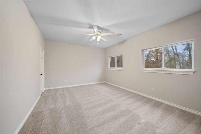 carpeted empty room with baseboards, a ceiling fan, and visible vents