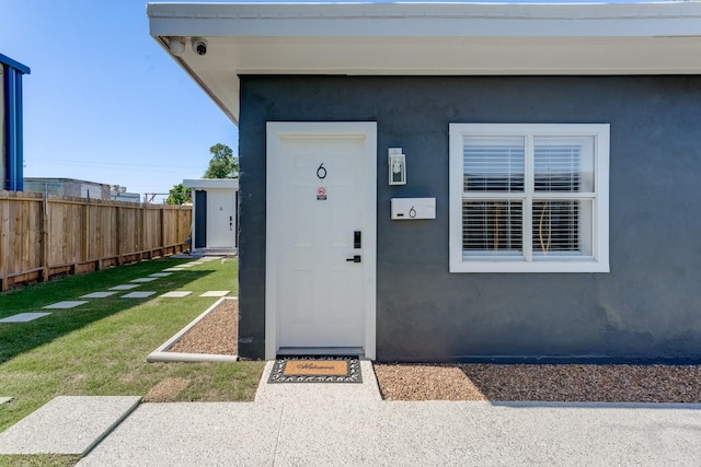 property entrance with fence, a lawn, and stucco siding