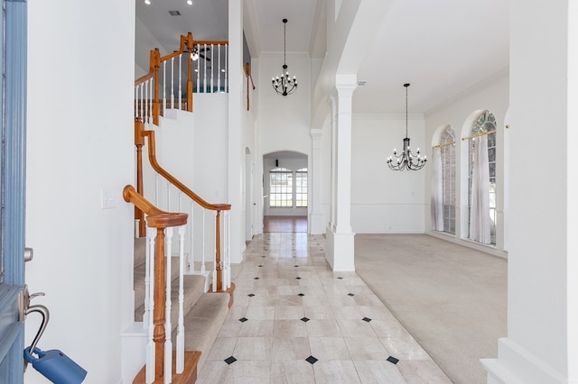 entryway featuring arched walkways, an inviting chandelier, ornamental molding, decorative columns, and stairs