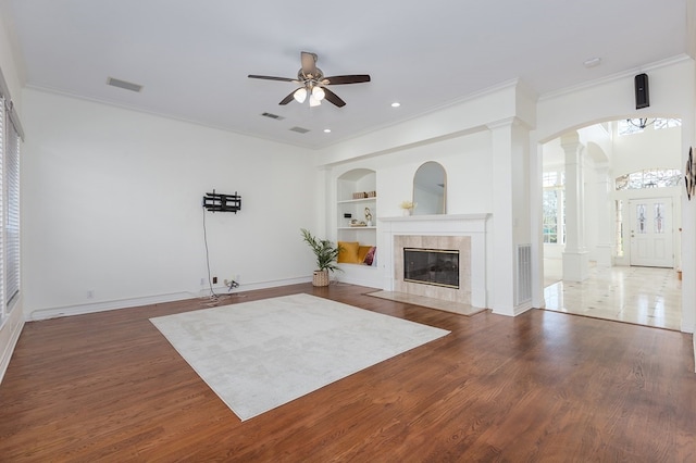 unfurnished living room featuring built in features, ornamental molding, decorative columns, a ceiling fan, and a tile fireplace