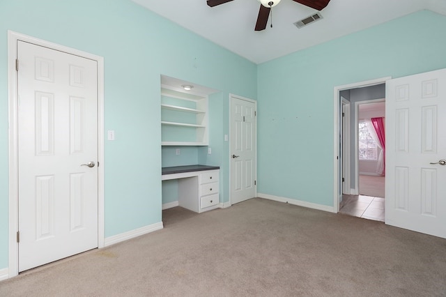 unfurnished bedroom with visible vents, baseboards, built in desk, ceiling fan, and light colored carpet