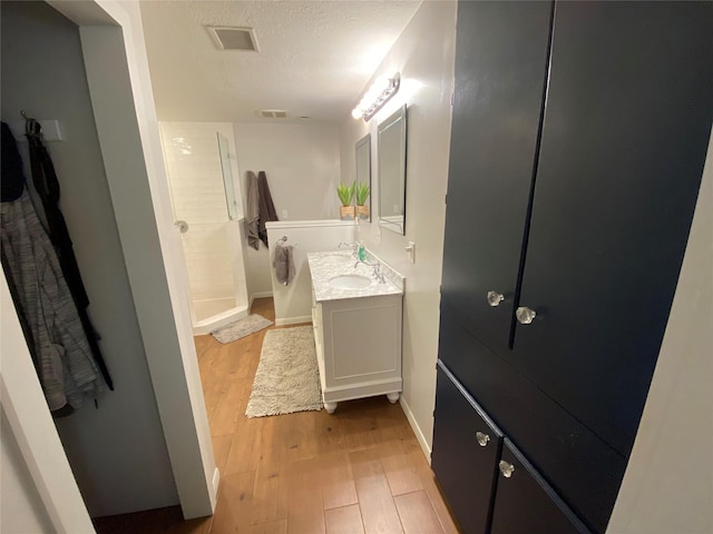 bathroom with visible vents, walk in shower, baseboards, vanity, and wood finished floors