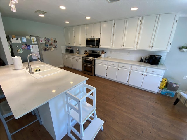 kitchen featuring stainless steel appliances, a sink, dark wood-style flooring, white cabinetry, and a breakfast bar