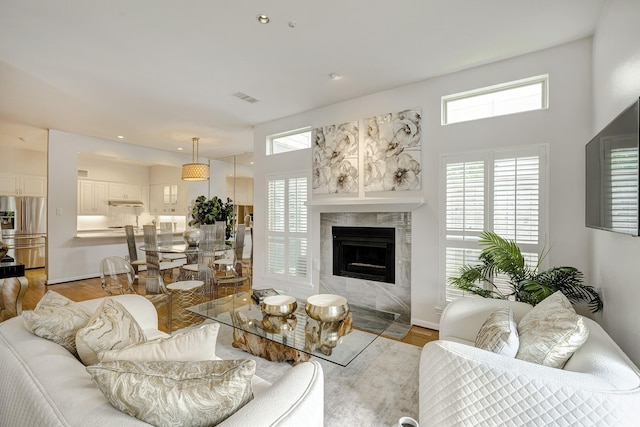 living area with recessed lighting, light wood-type flooring, a high end fireplace, visible vents, and a towering ceiling