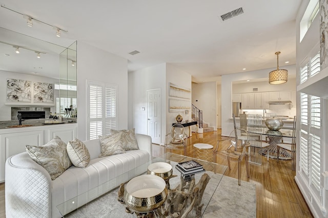 living area with stairway, rail lighting, a fireplace, light wood finished floors, and visible vents