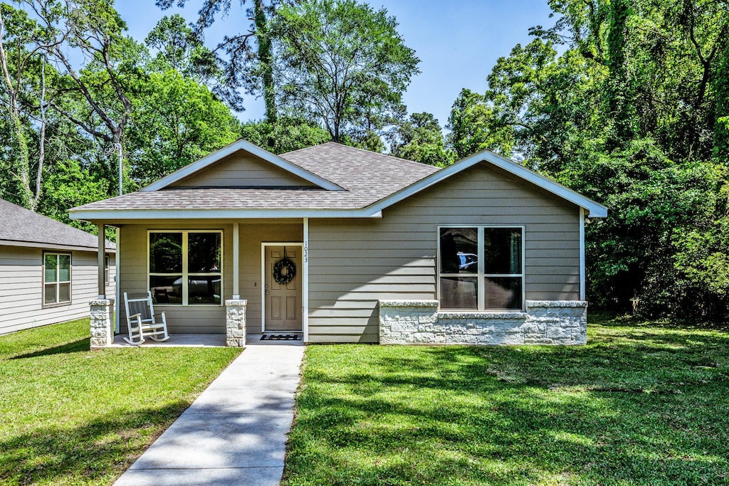bungalow-style house with a shingled roof, covered porch, and a front yard