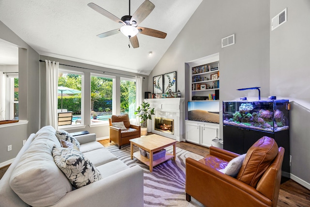living area featuring a premium fireplace, wood finished floors, visible vents, and ceiling fan