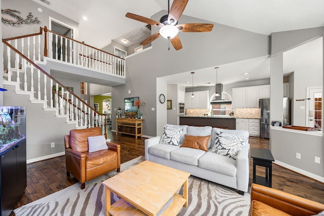 living room featuring ceiling fan, stairs, a towering ceiling, and dark wood-type flooring