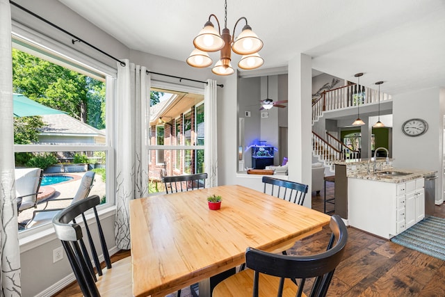 dining room featuring stairway, dark wood-style flooring, ceiling fan with notable chandelier, and a healthy amount of sunlight