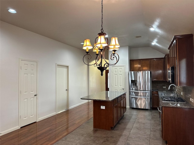 kitchen with a center island, dark stone counters, vaulted ceiling, a chandelier, and appliances with stainless steel finishes