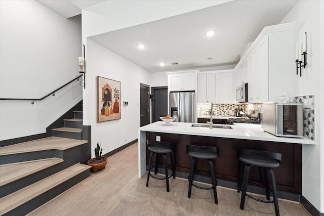 kitchen featuring a sink, appliances with stainless steel finishes, a peninsula, light wood finished floors, and white cabinetry