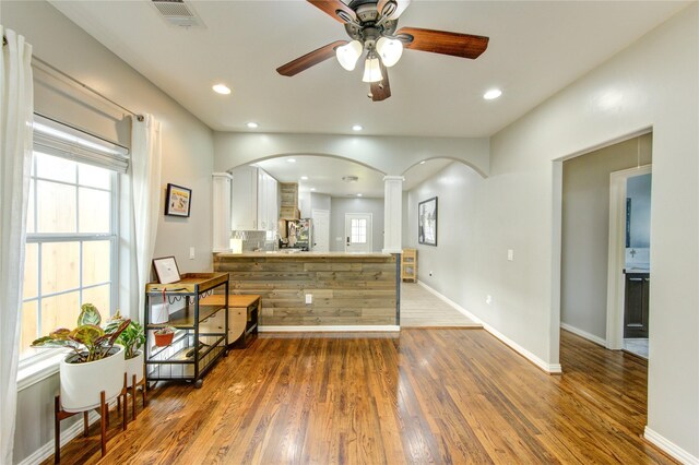 bar area with ornate columns, a ceiling fan, wood finished floors, arched walkways, and baseboards