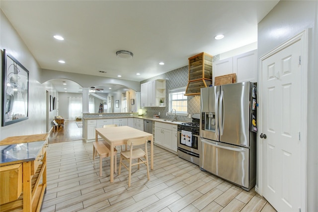 kitchen featuring stainless steel appliances, a sink, arched walkways, open shelves, and backsplash