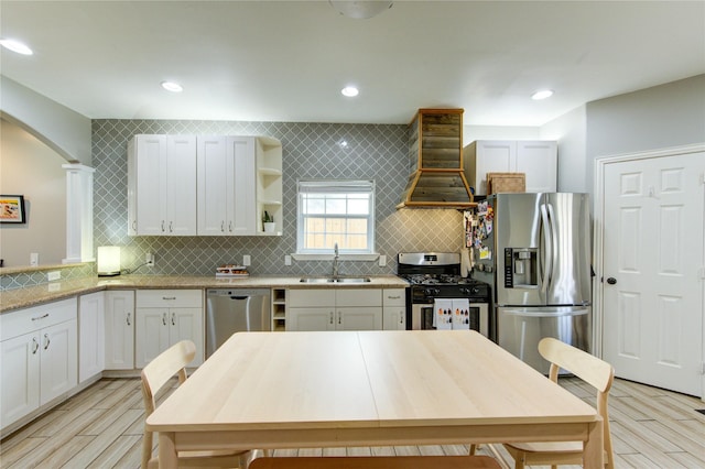kitchen with appliances with stainless steel finishes, a sink, custom exhaust hood, open shelves, and light wood finished floors