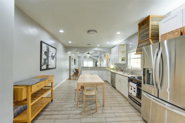 kitchen featuring appliances with stainless steel finishes, a sink, tasteful backsplash, white cabinets, and open shelves