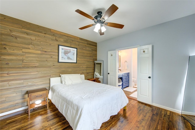 bedroom with wooden walls, dark wood-style floors, ensuite bathroom, baseboards, and a ceiling fan