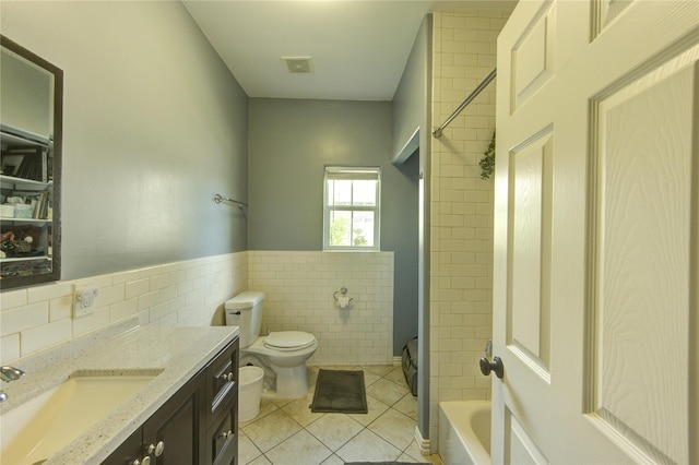 bathroom with tile walls, tile patterned floors, toilet, vanity, and washtub / shower combination