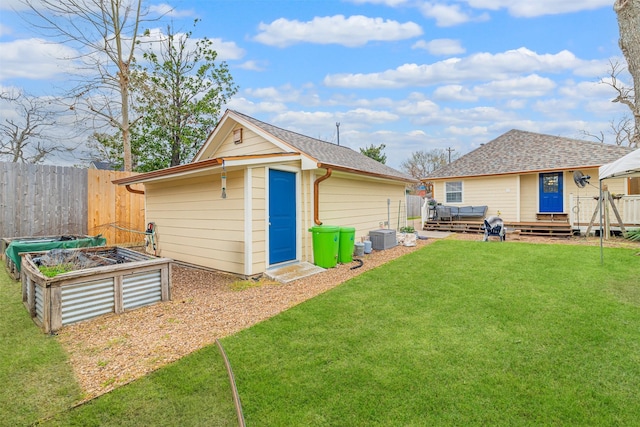 back of property featuring a vegetable garden, an outdoor structure, a wooden deck, and a shingled roof