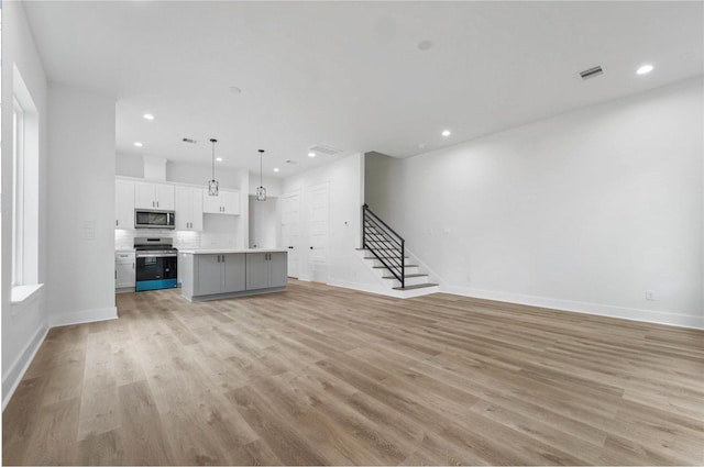 unfurnished living room with light wood-type flooring, baseboards, and stairs