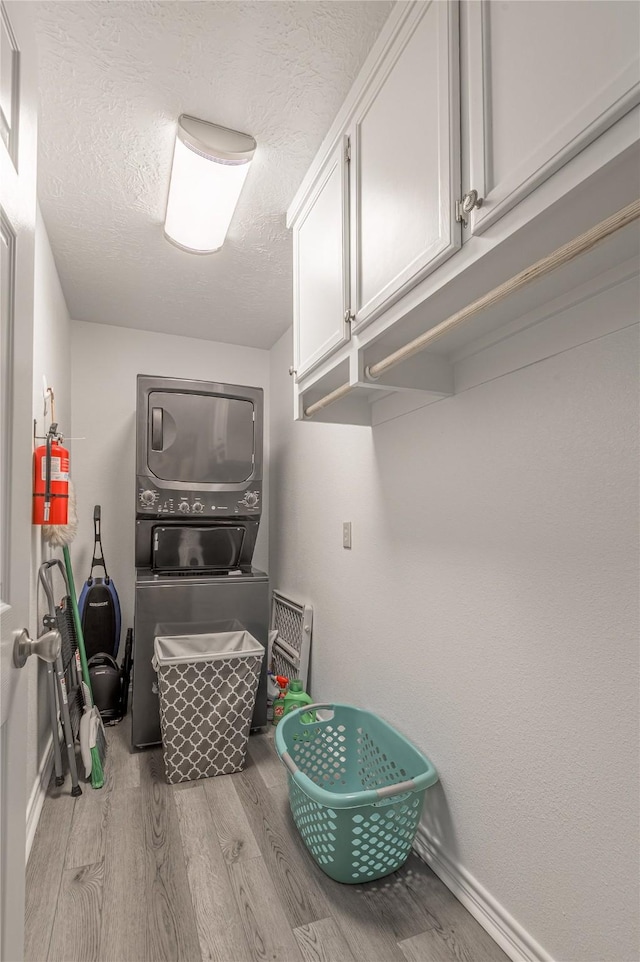 laundry area with baseboards, a textured ceiling, stacked washer and dryer, wood finished floors, and cabinet space