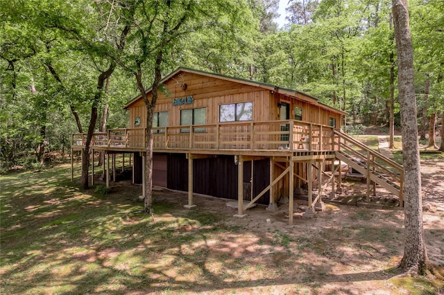 back of property with stairs, a wooden deck, a view of trees, and an attached garage