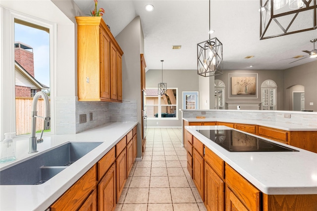 kitchen featuring brown cabinetry, a spacious island, a sink, decorative backsplash, and black electric stovetop