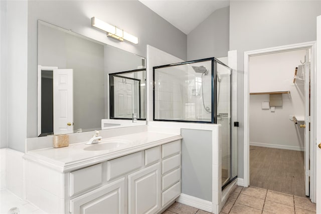 bathroom with a walk in closet, tile patterned floors, a shower stall, vaulted ceiling, and vanity
