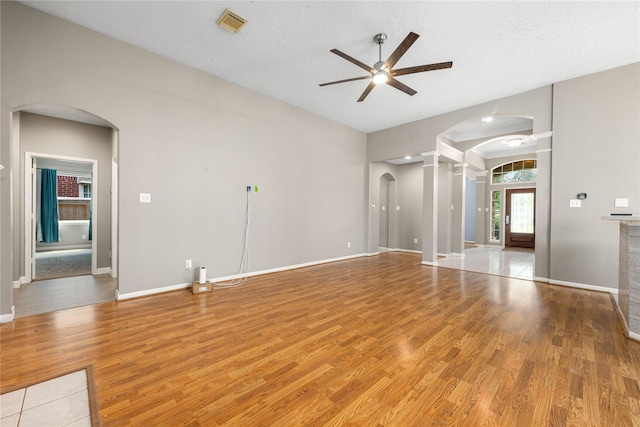 unfurnished living room with a ceiling fan, light wood-type flooring, visible vents, baseboards, and arched walkways