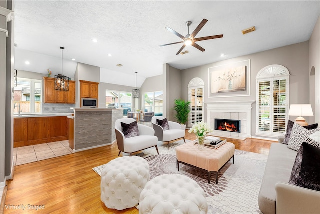 living area with a ceiling fan, light wood-style floors, a fireplace, and visible vents