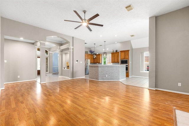 unfurnished living room featuring arched walkways, light wood-style flooring, ceiling fan, and decorative columns