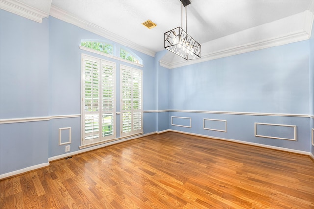empty room with visible vents, an inviting chandelier, crown molding, and wood finished floors
