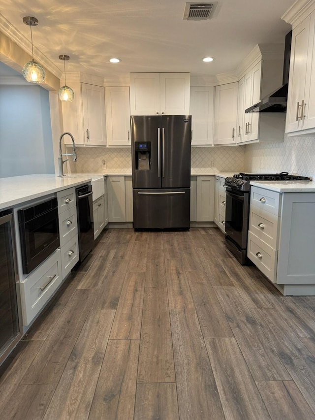 kitchen with light countertops, wall chimney range hood, visible vents, black appliances, and dark wood-style flooring