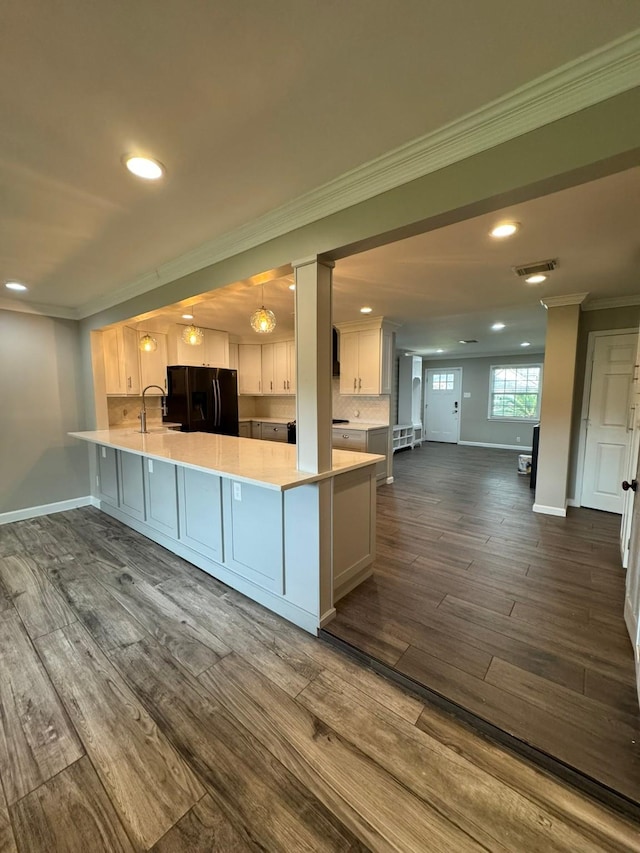 kitchen with a peninsula, dark wood finished floors, black fridge, crown molding, and light countertops