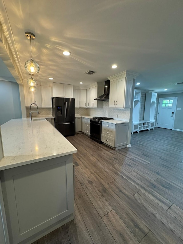 kitchen with black refrigerator with ice dispenser, wall chimney range hood, a sink, gas range, and a peninsula